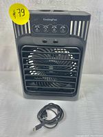 Front view of the black portable cooling fan showing front grille, fan blades, control panel with four buttons, and included USB Type-C cable in front.