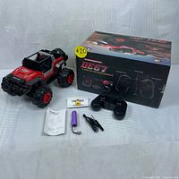Photo showing the DEERC DE67 off-road vehicle, its original box, black remote control, purple rechargeable battery, charging cables, manuals, and caution signs.