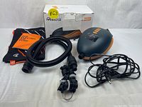 Photo showing the OutdoorMaster Dolphin electric SUP air pump, black flexible hose, multiple nozzle attachments, power cord, orange and black carrying pouch with 'SUP Electric Air Pump' label, and the original OutdoorMaster box.