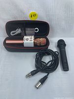 Wireless karaoke microphone inside a black zippered case with USB charging cable; wired microphone beside it with attached cable