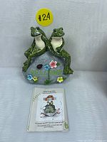 Frog couple statue seated on a rock with 'WELCOME' and colorful flowers, alongside instruction manual.