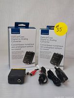 Two boxed Insignia digital to analog audio converters with accompanying cables and power cords, placed on a yellow surface.