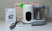 Front view of Bear baby food maker unit with user manual and original box in background.