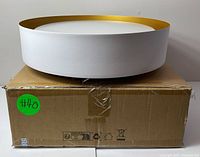 Front view of round white ceiling light with gold rim sitting on a cardboard box.