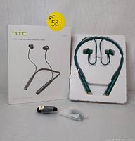 Front view of HTC H501 headset with packaging, showing green wireless neckband headphones, USB-C charging cable, and additional ear tips still in small sealed bag.