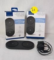 Two boxed Insignia 20W Dual-Device Qi Wireless Charging Stations with one charging station and one power adapter out in front.