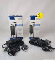 Two boxed Insignia universal laptop chargers, one 90W and one 65W, alongside their cables and multiple adapter tips in small bags shown in front of boxes.