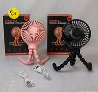 Pack of 2 new Versatile Handheld Stroller Fans in pink and black colors with boxes and USB cables included.