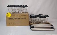 Full set of 8 solar pathway lights, some in original cardboard box, others disassembled showing stakes and light units.