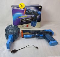 Photo showing the blue electric water gun, circular magazine, charging cable, and box in the background.