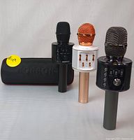 Photo showing the set of three Bonaok wireless Bluetooth karaoke microphones in black, white with rose gold accents, and black with grey accents, alongside the black carrying case.