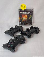 Three black DualShock 3 wireless controllers placed in front of the Minecraft PlayStation 3 Edition game case showing the front cover art.