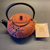Full view of red cast iron teapot with handle and tag