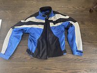 Front view of blue, black, and white motorcycle jacket laid flat on wood floor