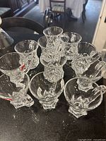 Group of nine clear glass punch bowl cups with handles arranged in a circle on a black countertop.