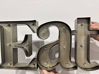 Close-up photo showing metal letter 'A' with multiple clear light bulbs attached on the front surface. The letter is hollow inside and made of silver/grey metal with some wear.