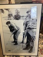 Framed black and white photographic print showing Fidel Castro and Che Guevara golfing in fatigues, held upright showing full print and frame.