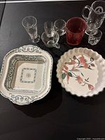 Overview photo showing floral ceramic pie dish with scalloped edge and additional ceramic serving dish with blue-green border patterns alongside a collection of clear and red glassware items