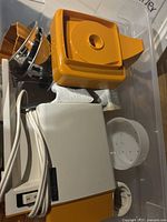 Overview photo showing the main meat grinder body with power switch, orange hopper, metal grinding parts, and other attachments.