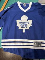Blue Toronto Maple Leafs hockey jersey laid flat, showing front design with large white maple leaf and team text