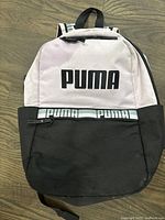 Full view of Puma backpack showing light pink top section and black lower section with large PUMA logo.