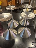 Four stainless steel martini glasses upside down showing the conical base and brushed metal finish.