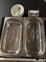 Top view of two stainless steel chafing dishes with clear lids and other items such as a small jar and tin box in the background