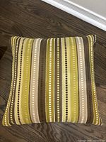 Front view of one striped decorative pillow showing yellow, brown, beige vertical stripes and small square dot pattern.