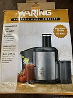 Front view of the Waring juice extractor box showing product image, brand name, and key features including 850-watt motor, two-speed operation, and extra wide 3-inch feed tube.