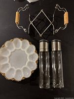 Top view of the white devilled egg dish, salt and pepper grinders, and metal trivet with wooden handles all arranged on a black surface.