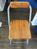 Wooden stool with natural wood seat and backrest with silver metal frame showing wear on floor