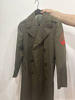 Front view of WWII olive green wool military coat hanging on hanger, showing double-breasted button front and lapels. Size 38 Regular.
