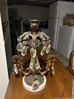 Front view of the vintage brass candleholder with crystal drops and round white base showing overall condition.