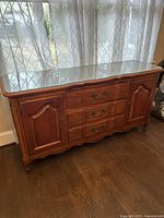 Front view of the traditional wood sideboard showing the medium wood tone finish, ornate metal handles, three central drawers, two side cabinets and carved feet.