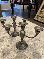 Pair of traditional metal candelabras with three holders each placed on a textured rug.