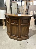 View of the closed corner cabinet showing brown wood finish and traditional panel detailing with a single drawer and cupboard door