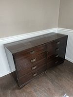 Full view of the dark brown wooden 6-drawer dresser in an empty room, showing its size and shape.