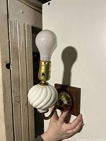 Wall sconce held by hand showing full height, brass fixture, and white porcelain spiral decorative piece with bulb installed.
