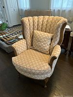 Front view of vintage wingback chair showing curved armrests, patterned fabric upholstery, wooden legs, and matching cushion