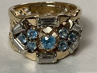 Front view showing central round blue topaz, six smaller round blue topaz and four baguette diamonds in lattice setting
