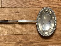 Top-down view of oval silver bowl and part of handle on wood floor