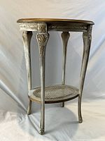 Front view of oval side table showing overall shape, carved legs, and lower caned shelf