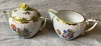 Front view of sugar bowl with lid and creamer side by side, showing floral and butterfly motifs and gold accents