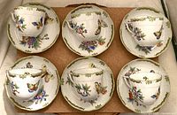 Overhead view of all six coffee cups placed on matching saucers, board background