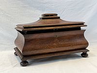 Three-quarter front view of closed tea caddy showing sarcophagus shape, bombe sides, stepped lid and bun feet