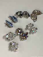 Overhead view of multiple pairs of clip-on earrings in various rhinestone cluster designs and colors on white background