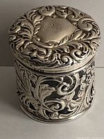 Front and side view showing intricate hand-crafted sterling silver scroll and floral design with face motif on lager crystal box.