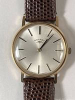 Front view of watch showing silver dial, gold case and brown leather strap