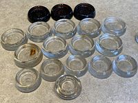 Top view showing arrangement of all 22 vintage glass furniture coasters in amber and clear glass. Coasters vary in size with some amber colored and clear glass pieces visible.