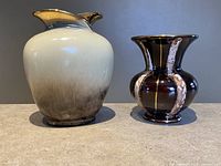 Photo of two mid-century West German ceramic vases, one cream and brown gradient with dual spouts, the other dark glossy with flared rim.